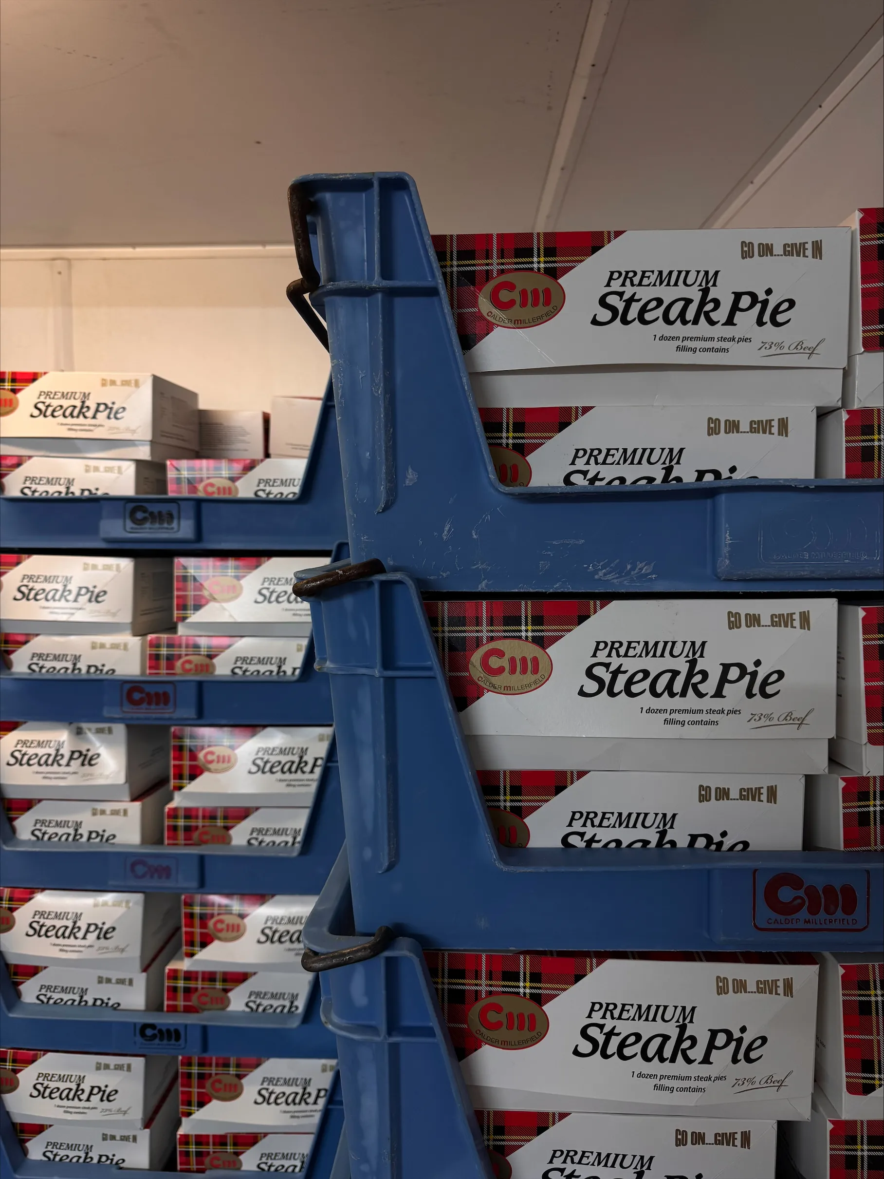 Cases of Calder Millerfield Premium Steak Pies stacked on blue shelving racking.