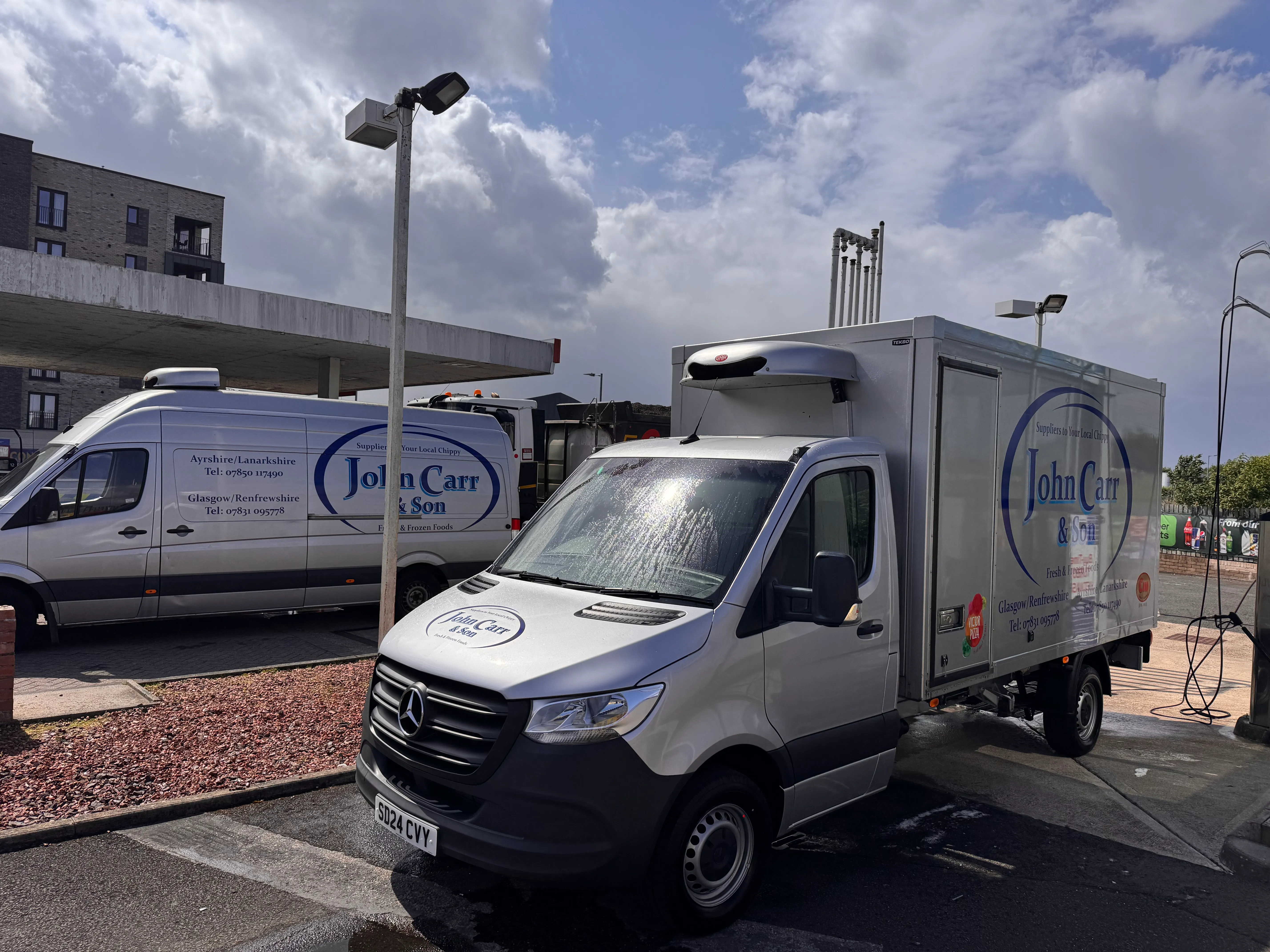 Two John Carr & Son branded delivery vans parked together, showing the "Suppliers to Your Local Chippy" and "Fresh & Frozen Foods" livery.