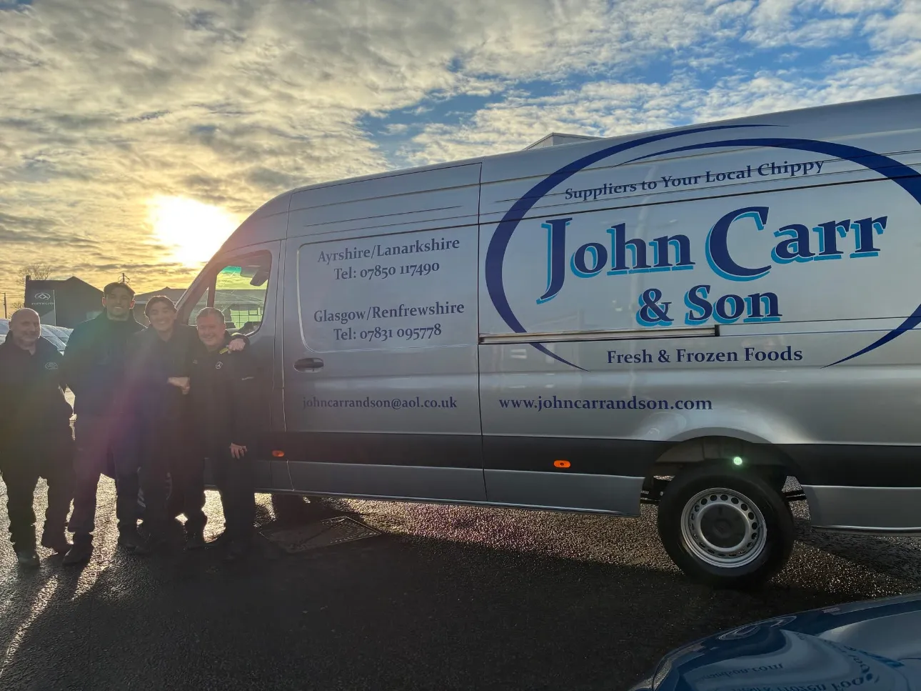 The John Carr & Son team standing together beside a branded delivery van at sunset.